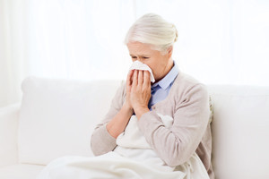 sick senior woman blowing nose to paper napkin